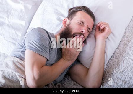 Morgens wach Mann Bett gähnend weit Stockfoto