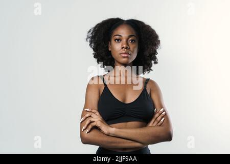 Junge schwarze Frau in Sportkleidung posiert und schaut isoliert auf weißem Hintergrund auf die Kamera Stockfoto
