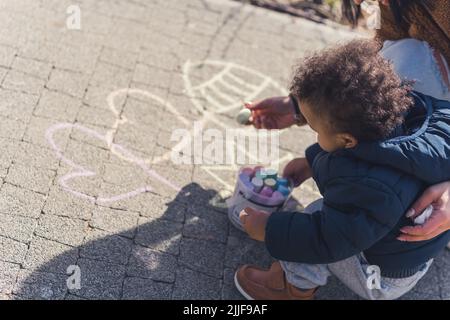 Ein kleiner schwarzer Junge, der mit Buntstiften auf dem Bürgersteig zeichnet. Hochwertige Fotos Stockfoto