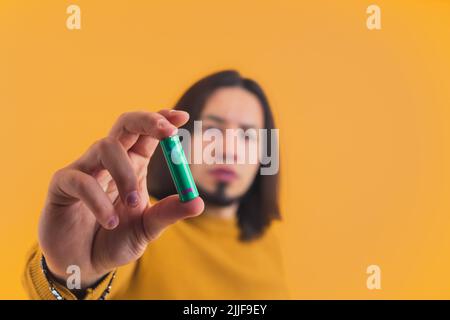 Hispanischer, seriös aussehender Mann in seinem 30s in einem Studio stehend, der grüne Batterie zeigt und für sie wirbt. Hochwertige Fotos Stockfoto