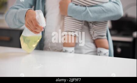 Ich und mein Kind in Sicherheit zu halten. Eine Mutter putzt ihre Küchentheke, während sie ihr Baby hält. Stockfoto