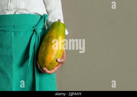 Nahaufnahme einer Frau, die eine Papaya vor einfachem Hintergrund hält - Stockfoto Stockfoto
