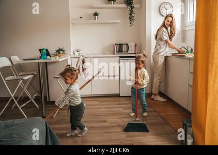 Kleine Mädchen helfen ihren weiblichen Eltern, die Küche zu reinigen Stockfoto