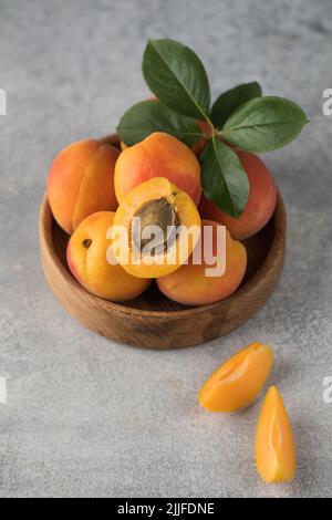 Reife saftige Aprikosen auf einem Holzteller auf grauem Grund. Frisches Obst . Stockfoto
