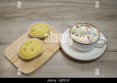 Zwei Muffins mit Rosinen auf einem Holztablett und einer Tasse heiße Schokolade Stockfoto