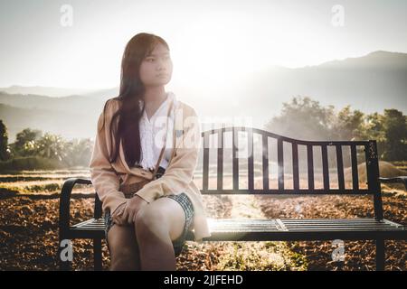 Ein Mädchen sitzt an einem Herbstmorgen auf einer Bank inmitten eines ländlichen Feldes Stockfoto