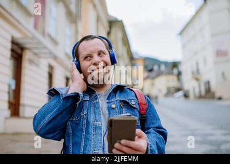 Fröhlicher junger Mann mit Down Sydrome, der Musik hört, wenn er auf der Straße läuft. Stockfoto
