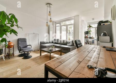 Einfache offene Küche mit weißen Schränken und Wohnzimmer mit grauem Sofa bei Tageslicht Stockfoto