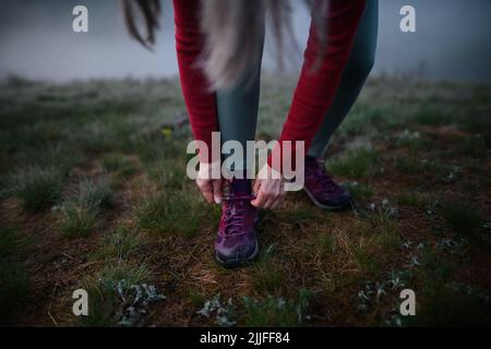 Nahaufnahme einer älteren Frau, die ihre Schnürsenkel schnürte, bevor sie am frühen Morgen mit Nebel in der Natur Sport machte. Stockfoto