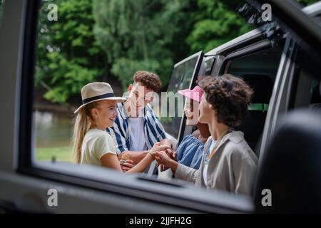 Multirassische junge Freunde, die mit dem Auto zusammen reisen, mit dem Auto stehen und lächeln - Sommerurlaub, Urlaub, Reisen, Roadtrip und People-Konzept. Stockfoto