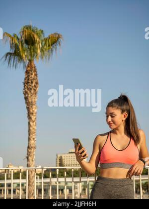 Schönes sportliches Mädchen, das sich nach dem Training mit der Smartphone-Running-App auf ein Geländer stützt Stockfoto