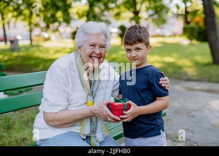 Das Enkelkind überraschte ihre Großmutter mit einem Geburtstagsgeschenk im Park. Lifestyle, Familienkonzept Stockfoto