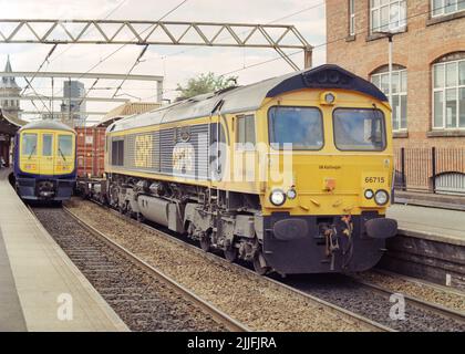 Manchester, Großbritannien - 2022. Juni: Eine Diesellokomotive (Klasse 66 66715) zog einen Containerzug am Deansgate-Bahnhof vorbei, einem Passagierzug im Heck. Stockfoto