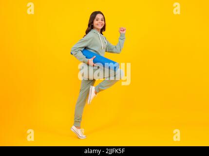 Laufen und springen. Mädchen Teenager im Trainingsanzug. Fröhliches, niedliches Kind in einem gelben Sportanzug auf gelbem Hintergrund. Sportbekleidung Werbekonzept. Stockfoto