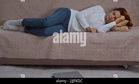 Rothaarige Frau, die im Wohnzimmer neben dem Laptop auf der Couch lappte Stockfoto