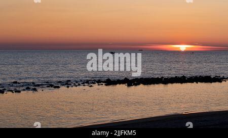 Wunderschöner pastellfarbener Sonnenuntergang am Strand, ein golden klarer Himmel und türkisfarbenes Meer mit Silhouetten von Fischerbooten im Hintergrund und am Horizont Sonne auf dem Meer Stockfoto
