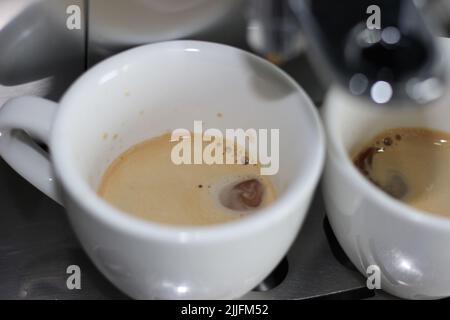 Espresso-Maschine, Kaffeebrau. Frischer Espresso tropft in zwei weiße Tassen. Morgenkaffee. Stockfoto