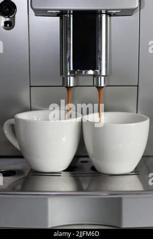 Frischer Espresso tropft in zwei weiße Keramikbecher. Kaffeebrau. Stockfoto