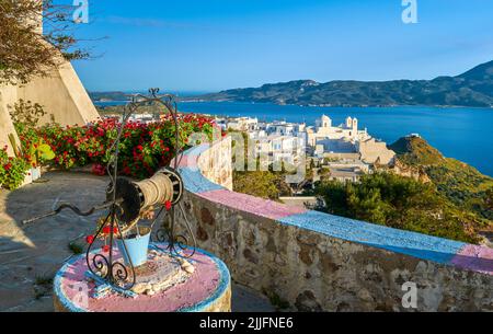 Farbenfrohe Aussicht auf die traditionelle griechische Stadt am Meer von der dekorierten Terrasse mit satten roten Kranichschnäbeln. Weiße orthodoxe griechische Kirche, Plaka, Milos, Griechenland Stockfoto