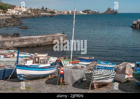 Alte Holzboote an einem Strand in Aci Castello, mit Aci Trezza im Hintergrund, Catania, Italien Stockfoto