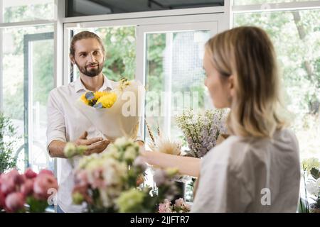 Ein junger bärtiger Mann kauft einen schönen Blumenstrauß für den Urlaub eines Mädchens in einem gemütlichen Blumenladen. Floristik und Blumenstrauß in einem Blumenladen. Kleinunternehmen. Stockfoto