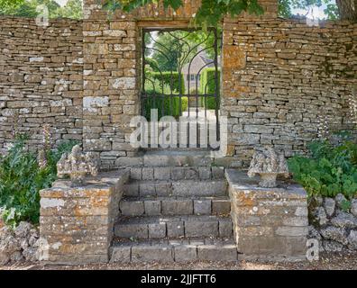 Steintreppe führt zu einem schmiedeeisernen Gartentor in einer traditionellen cotswold Steingartenmauer Stockfoto