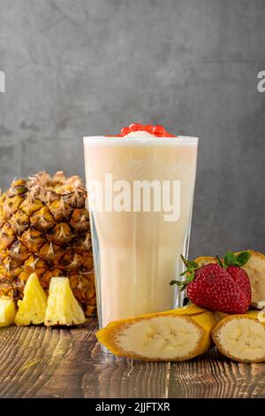Bananen-, Erdbeer- und Ananas-Smoothie auf dem Holztisch und Bubble Tea oder boba-Teebällchen darauf Stockfoto