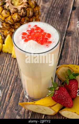 Bananen-, Erdbeer- und Ananas-Smoothie auf dem Holztisch und Bubble Tea oder boba-Teebällchen darauf Stockfoto