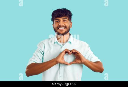 Porträt von fröhlich attraktiven indischen Kerl zeigt Liebe Geste auf hellblauem Hintergrund. Stockfoto