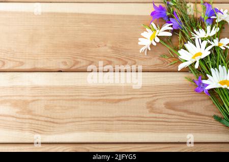 Ein Blumenstrauß aus Bluebells und Gänseblümchen auf einem hellen Holzhintergrund. Herzlichen Glückwunsch. Urlaub. Geburtstag. Ein flacher Kopierbereich mit Draufsicht. Stockfoto