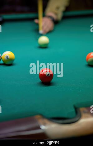 Nahaufnahme einer roten Kugel mit der Nummer 3. Die Hand eines Spielers mit einem Queue und Kugeln auf einem grünen Tuch auf einem unscharfen Hintergrund. Stockfoto