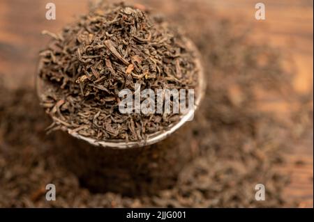 Schwarzer Tee mit großen Blättern in einem Glas und auf dem Tisch verstreut. Nahaufnahme der Oberflächenstruktur. Stockfoto