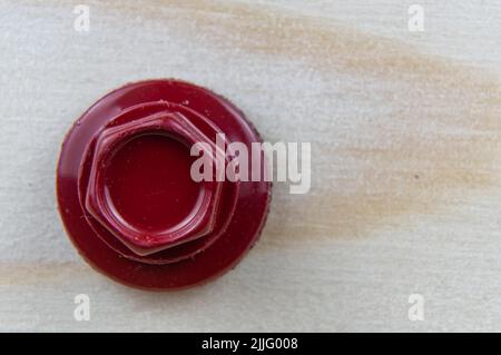 Nahaufnahme des Kopfes einer roten Blechschraube, die in eine Holzplatte geschraubt wurde. Platz für Text oder Logo. Stockfoto