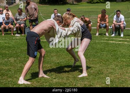 Ein junges Teenager-Mädchen, das mit einem Jungen kämpft, der beim Grand Cornish Wrestling Tournament auf dem malerischen Dorfgrün von St. Mawgan in Pydar i teilhat Stockfoto