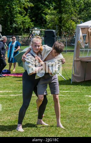 Ein junges Teenager-Mädchen, das mit einem Jungen kämpft, der beim Grand Cornish Wrestling Tournament auf dem malerischen Dorfgrün von St. Mawgan in Pydar i teilhat Stockfoto