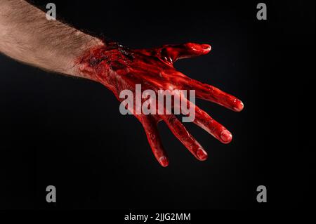 Nahaufnahme einer mit Blut befleckten männlichen Hand auf schwarzem Hintergrund. Stockfoto