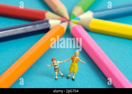 Miniatur Menschen Spielzeug Figur Fotografie. Zeichnungsklassenkonzept. Eine Gruppe von Kindern, die auf farbigem Bleistift spielen, isoliert auf blauem Hintergrund. Bildfoto Stockfoto