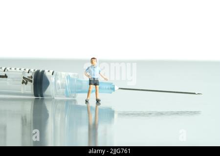 Miniatur Menschen Spielzeug Figur Fotografie. Impfkonzept für Kinder. Ein Junge, der vor der Spritze steht, lädt ein, sich impfen zu lassen. Bildfoto Stockfoto