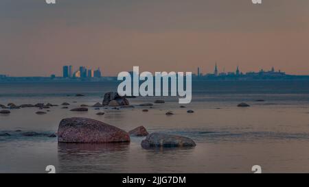 Felsen in der ruhigen Ostseeküste auf dem Hintergrund der Silhouette von Zentral-Tallinn. Fotografiert bei einem farbenfrohen Sonnenuntergang. Stockfoto