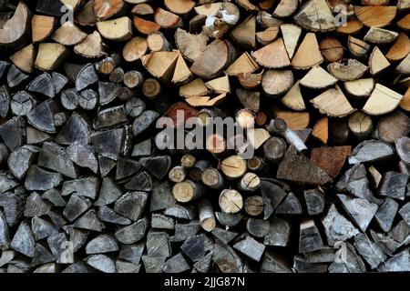 Ein Stapel frisch gehackter Holzstämme, die auf älteres, graues Brennholz aufgeschlagen sind. Stockfoto