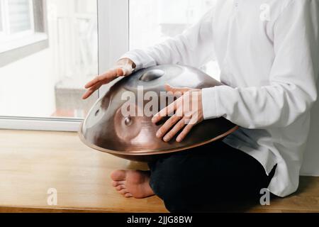 Mann, der auf der Hangdrum oder Steel Drum, Hangpan, einem modernen Musikinstrument aus Stahl zu Hause, spielt. Meditationsmusik zum Entspannen. Nahaufnahme Stockfoto