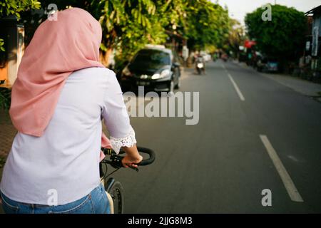 Rückansicht junge asiatische muslimische Frau beim Radfahren auf der Straße Stockfoto