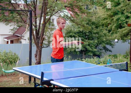 Blonde junge in roten T-Shirt spielen Tischtennis im Freien Stockfoto