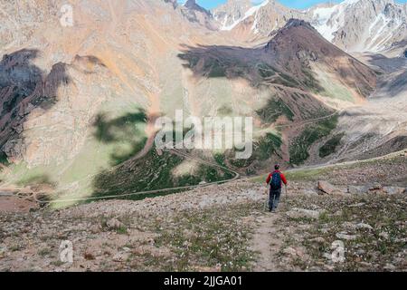 Ein Mann, der in einer roten Jacke unterwegs ist und einen atemberaubenden Blick auf die Berge genießt. Stockfoto