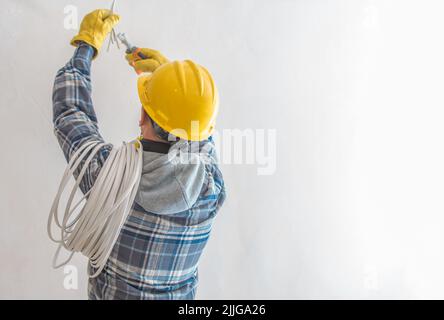 Professioneller Elektriker mit gelbem Harthut und Beleuchtung Installationsvorbereitung während der Renovierungsarbeiten Abisolieren der Drähte mit dediziertem Stockfoto