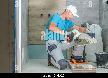 Kaukasischen Arbeiter in seinem 40s tun Renovieren im Badezimmer des Kunden Installation von hölzernen wie Keramikfliesen. Modernes Design. Thema Renovierungsarbeiten. Seite Stockfoto