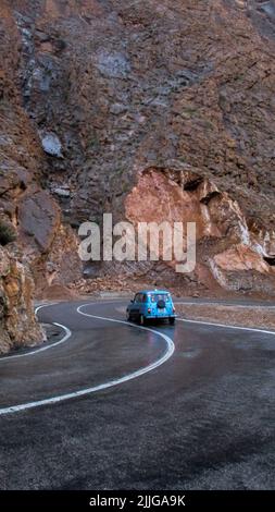 Eine Rückansicht des alten Autos, das in einer schmalen marokkanischen Straße fährt, die von Klippen umgeben ist Stockfoto