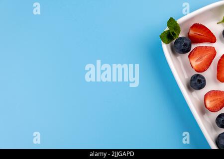 Teller mit Beeren und Minzblättern auf blauem Hintergrund, Vorlage zum Einfügen von Text, Menü. Hochwertige Fotos Stockfoto