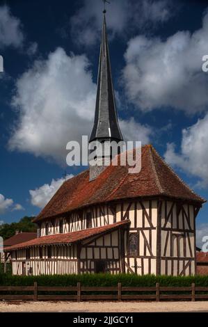 Ein schlanker schieferbedeckter Turm erhebt sich über dem rot gefliesten Dach der Fachwerkstatt Sainte-Croix-en-son-Exaltation in Bailly-le-Franc, einem kleinen Dorf in der Landschaft der Aube Pays du der in Grand Est, Frankreich. Die Kirche, die 1510 begann, wurde seit ihrer Errichtung kaum verändert und gehört heute zu den Attraktionen auf einer ausgeschilderten Tour durch die historischen Kirchen, Kapellen und Wohnungen der Champagne-Region mit Holzrahmen. Stockfoto