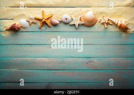 Ferien- und Sommerzeitkonzept mit Seesternen und Muscheln auf einem türkisfarbenen Holztisch mit Sand Stockfoto